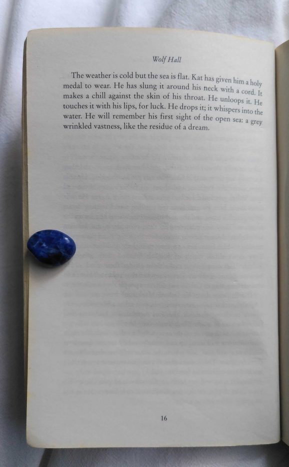 Page 16 of the book Wolf Hall by Hilary Mantel held open by a small blue stone