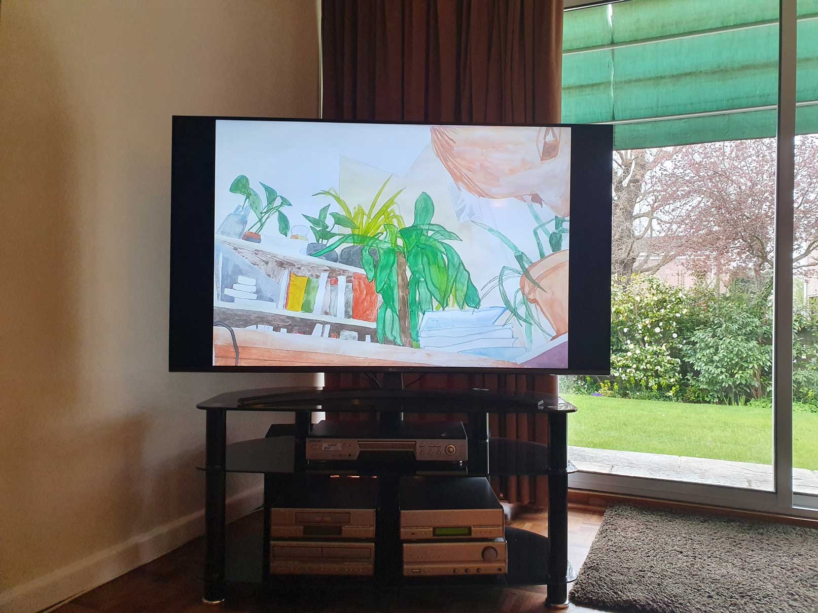 An image of a painting by the artist Alice Mendelowitz is displayed on a TV in the corner of a room, next to a glass sliding door that leads to a garden.