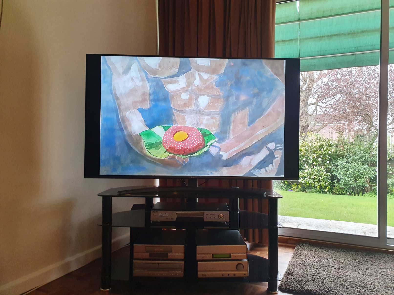 An image of a painting by the artist Alice Mendelowitz is displayed on a TV in the corner of a room, next to a glass sliding door that leads to a garden.